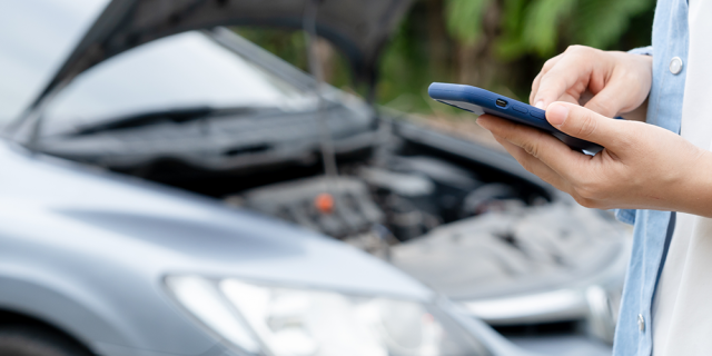 Persona revisa su celular, mientras en el fondo se observa un auto dañado