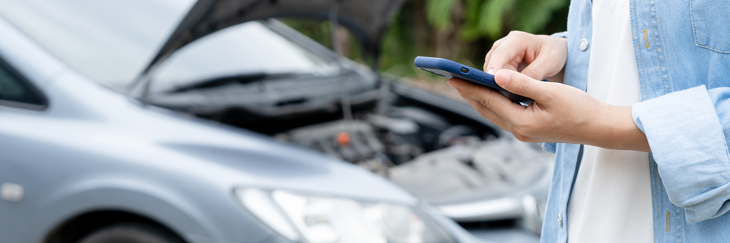 Persona revisa su celular, mientras en el fondo se observa un auto dañado